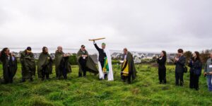 Sean O'Dowda Stephens raises the White Wand on the inauguration mound at Enniscrone, 9 October 2025, as cloaked clan members look on