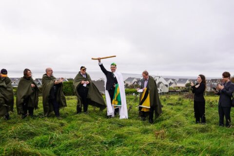 Sean O'Dowda Stephens raises the White Wand on the inauguration mound at Enniscrone, 9 October 2025, as cloaked clan members look on