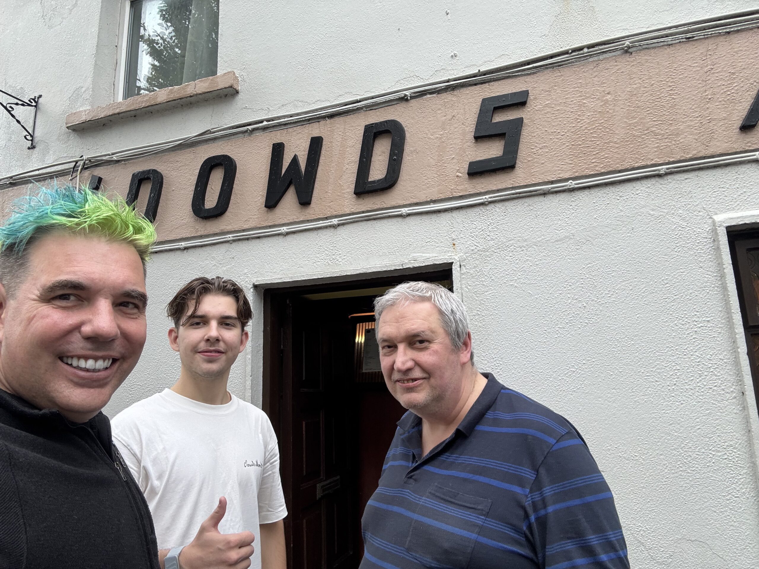 Three men outside Two O’Dowd’s pub in Ballina, beneath the painted O’DOWDS sign